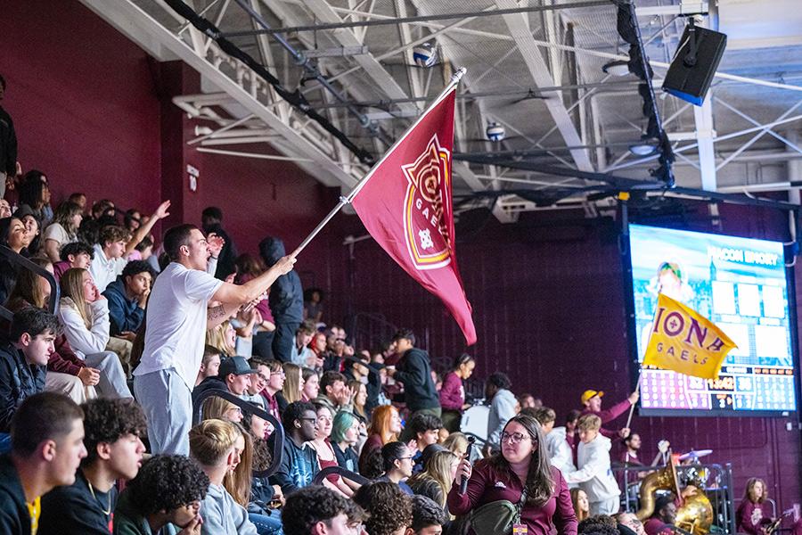 The student section cheering at a home basketball game and waving Iona flags.