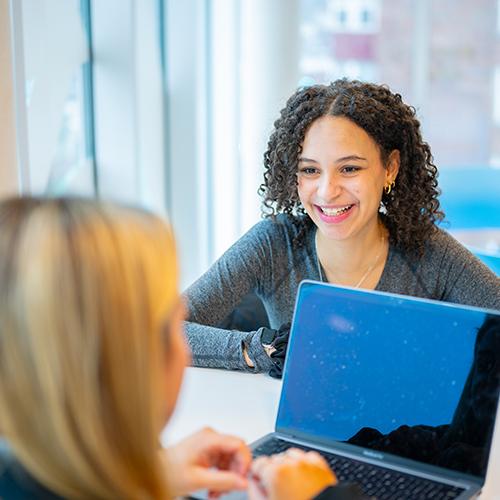 Two students study together and one of them smiles towards the camera.
