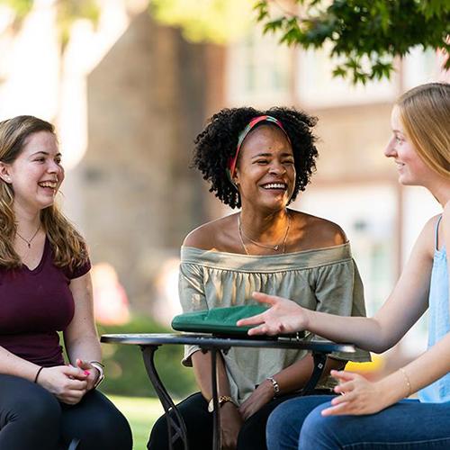 Three students talking outside at a table.