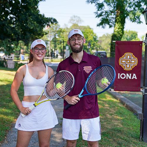 Two students with tennis rackets and tennis balls smile.