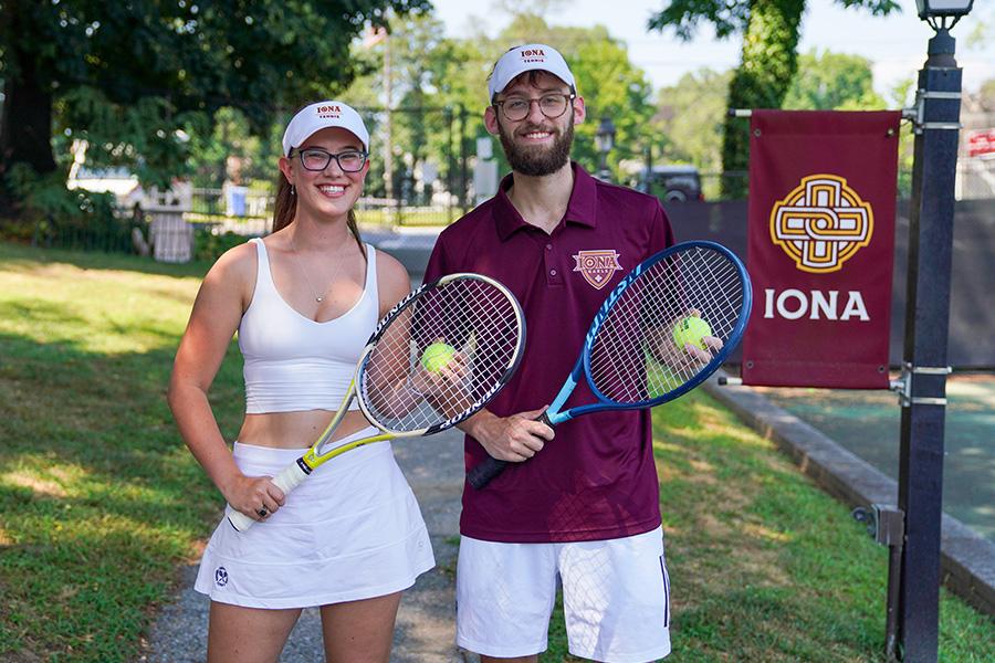 Two students with tennis rackets and tennis balls smile.