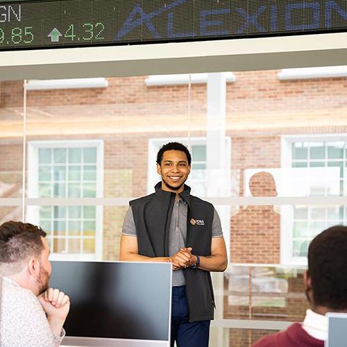 An MBA student presents in the trading floor room.