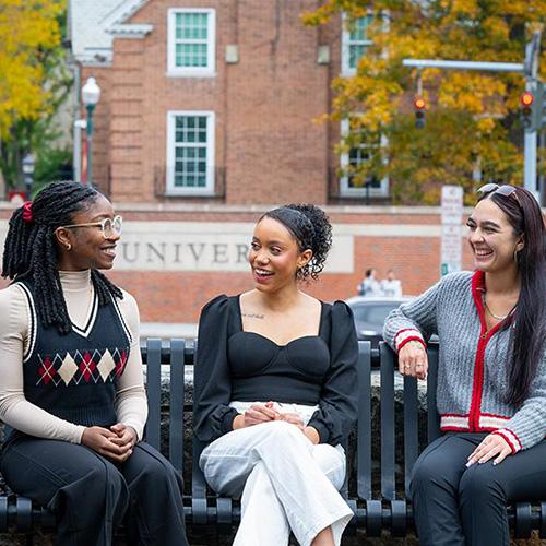 Three school psychologist students sit on a bench and talk.