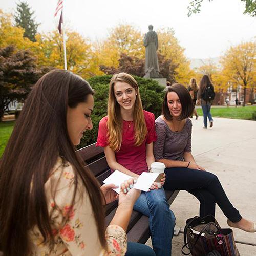 Three students study flashcards on a bench outside.