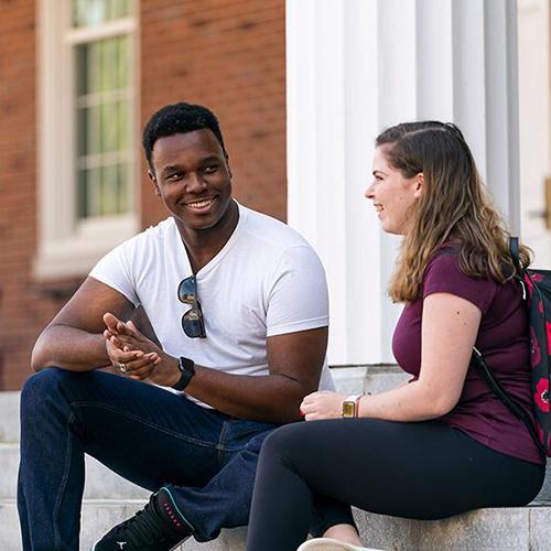 Two criminal justice students sit on the steps outside and talk.