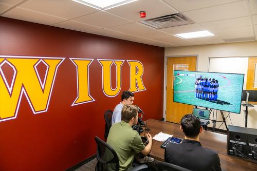 Three male students sitting in the Iona University radio room, and are live on the radio, broadcasting the Iona University Women's soccer game.