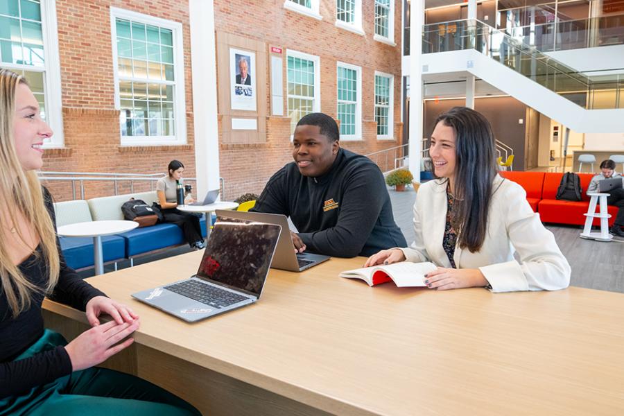Three students work at a table in the LaPenta School of Business.